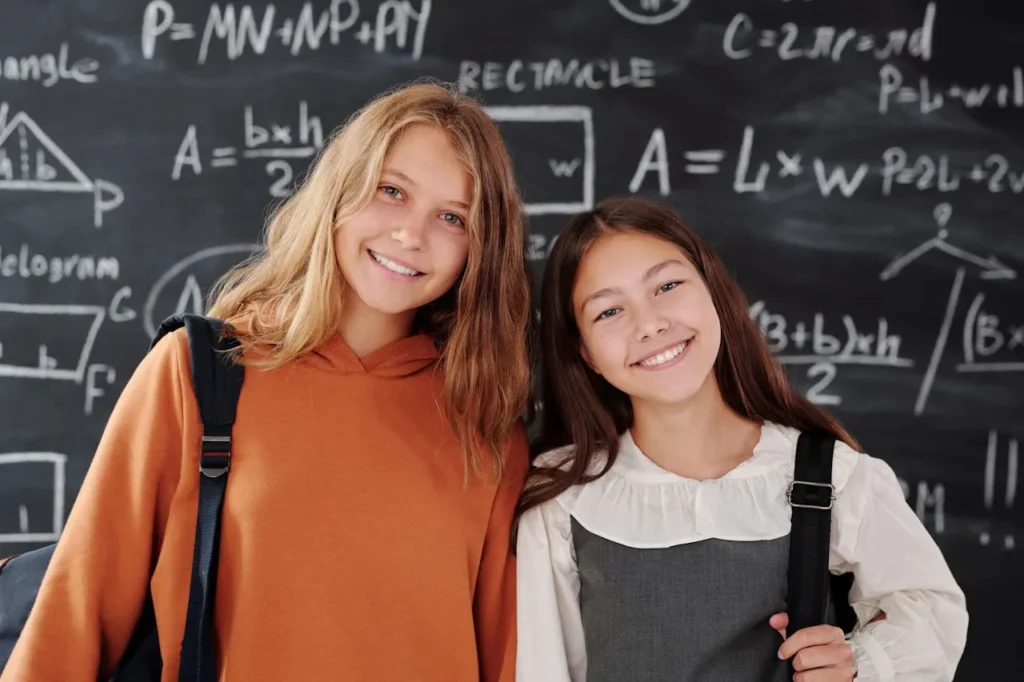 Two schoolgirls smiling in front of chalkboard with math formulas Two schoolgirls smiling in front of chalkboard with math formulas