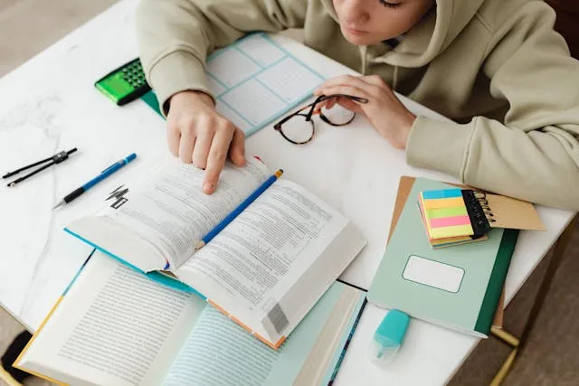 Student studying textbook and taking notes at desk Student studying textbook and taking notes at desk