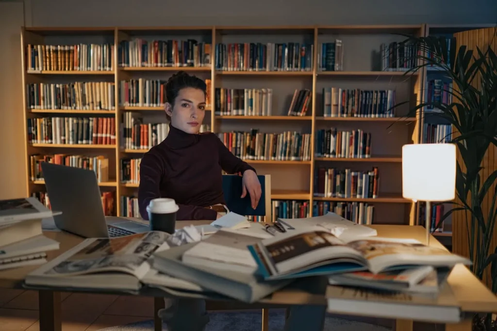 Woman studying in library with laptop and books