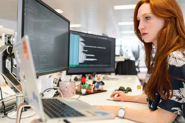 Woman programmer working at desk with multiple monitors Woman programmer working at desk with multiple monitors
