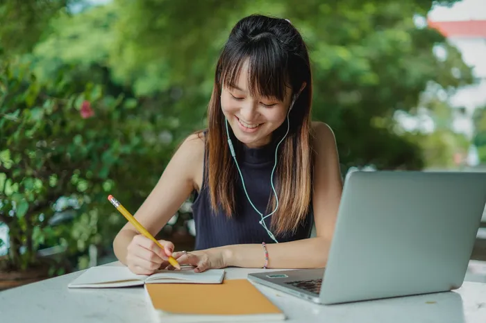 Student studying outdoors with a laptop and writing notes in a notebook